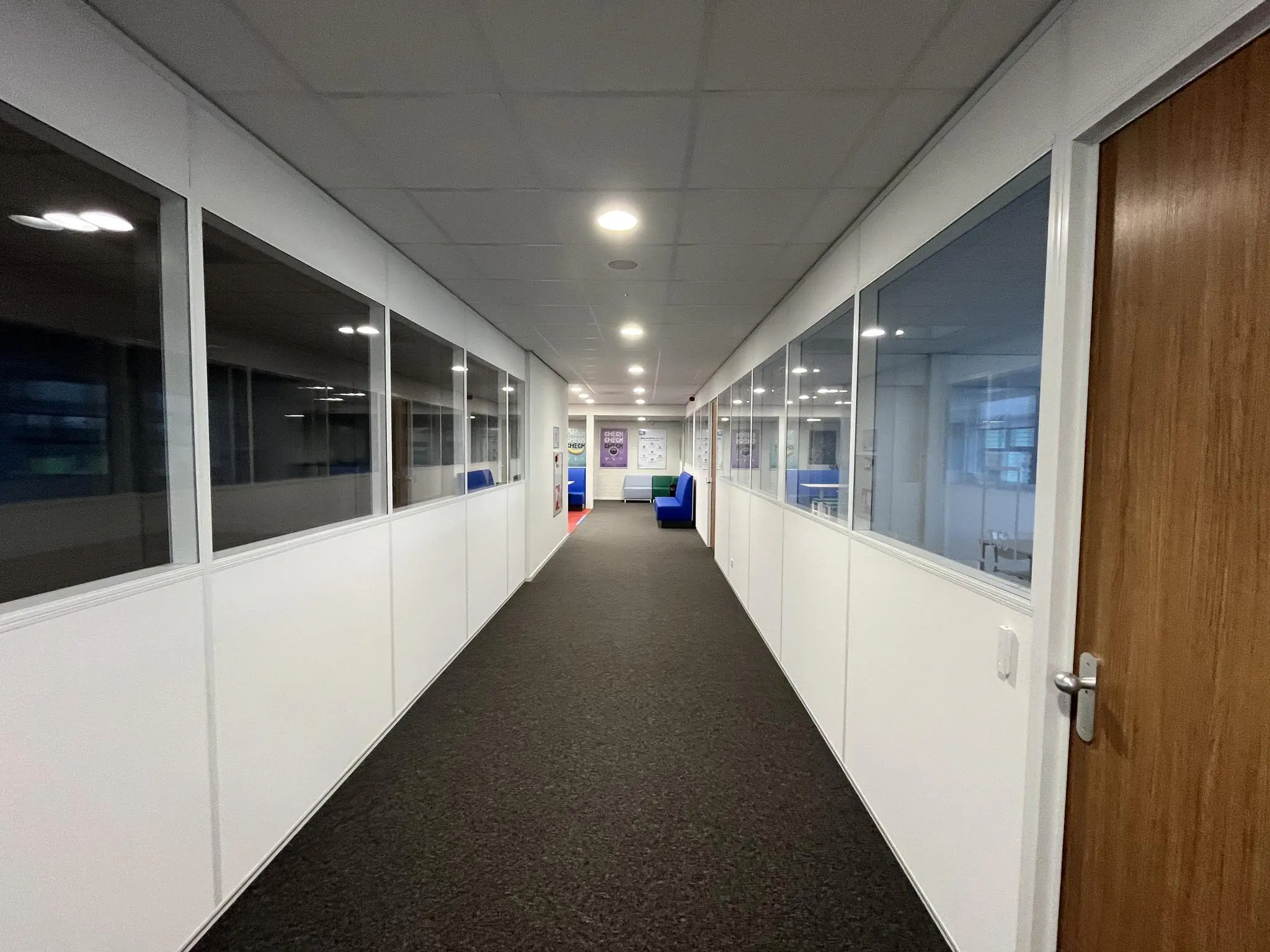 Lange, verlichte gang in een kantoorpand aan de Niels Bohrweg met glazen wanden en zicht op werkplekken.